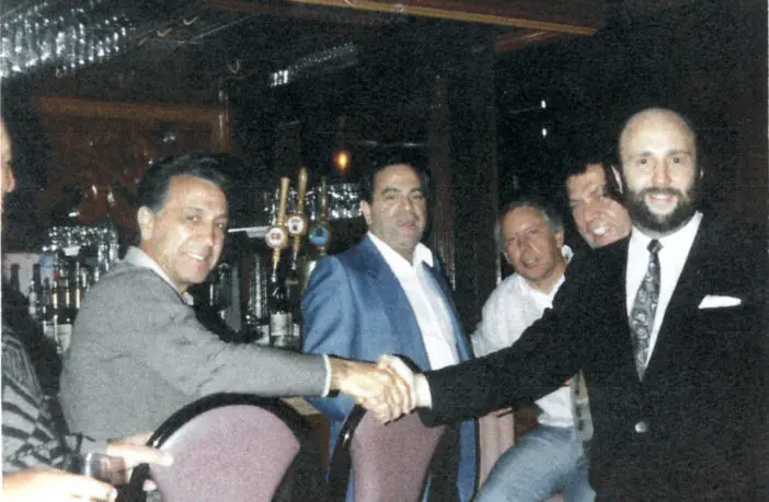 In a photo seized during a 1988 raid, mob boss John DiFronzo (far left) is seen shaking hands with a restaurateur. Marco D'Amico can just be seen peeking over the owner's shoulder.